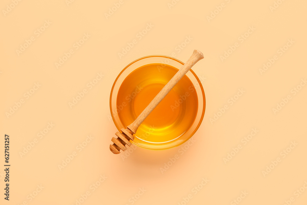 Glass bowl of sweet honey and dipper on beige background