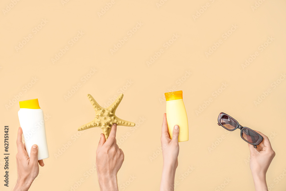 Female hands with bottles of sunscreen cream, starfish and sunglasses on beige background