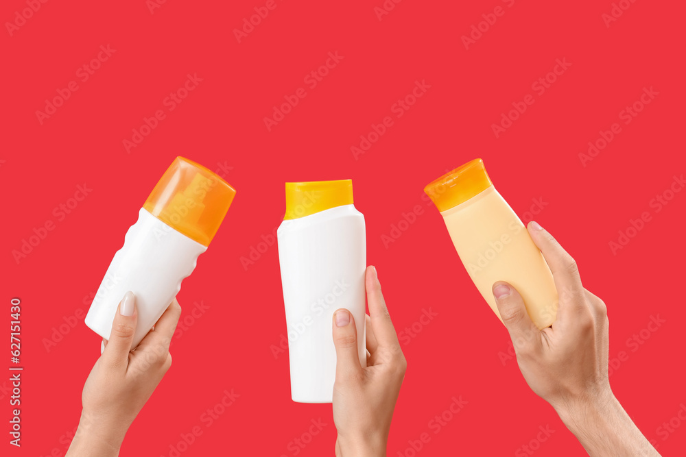 Female hands with bottles of sunscreen cream on red background