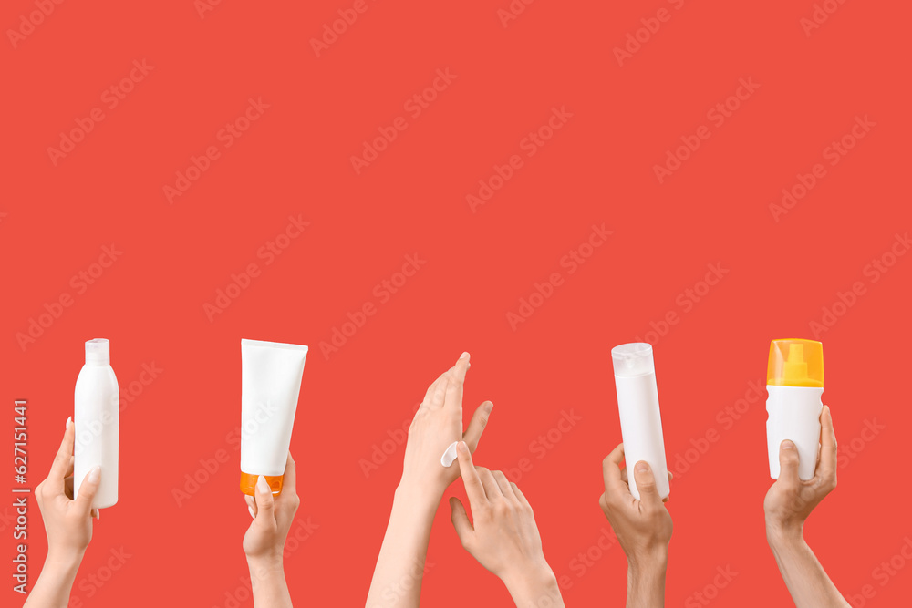 Female hands with bottles of sunscreen cream on red background