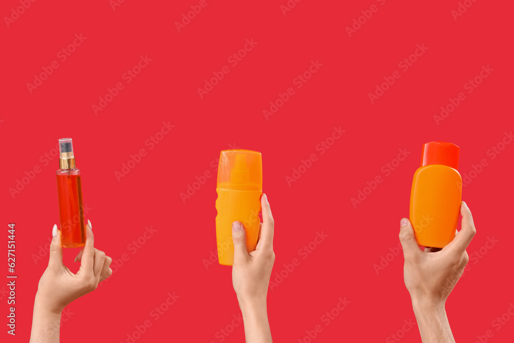 Female hands with bottles of sunscreen cream on red background