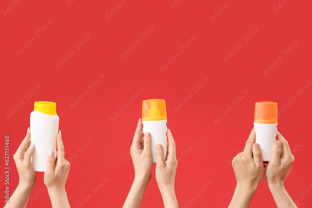 Female hands with bottles of sunscreen cream on red background