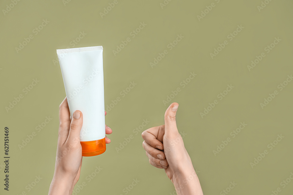 Female hands with bottle of sunscreen cream showing thumb up on green background