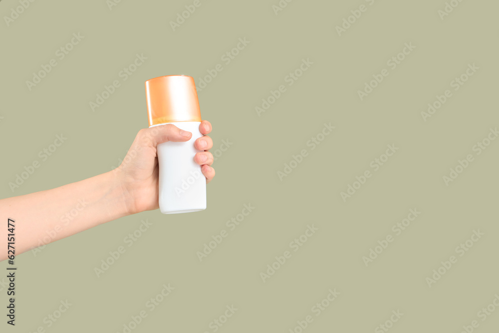 Female hand with bottle of sunscreen cream on green background