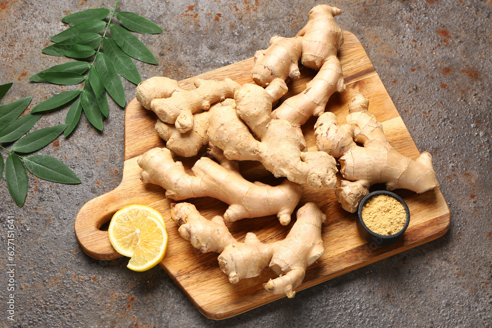 Wooden board with fresh ginger roots and bowl of dried powder on dark background