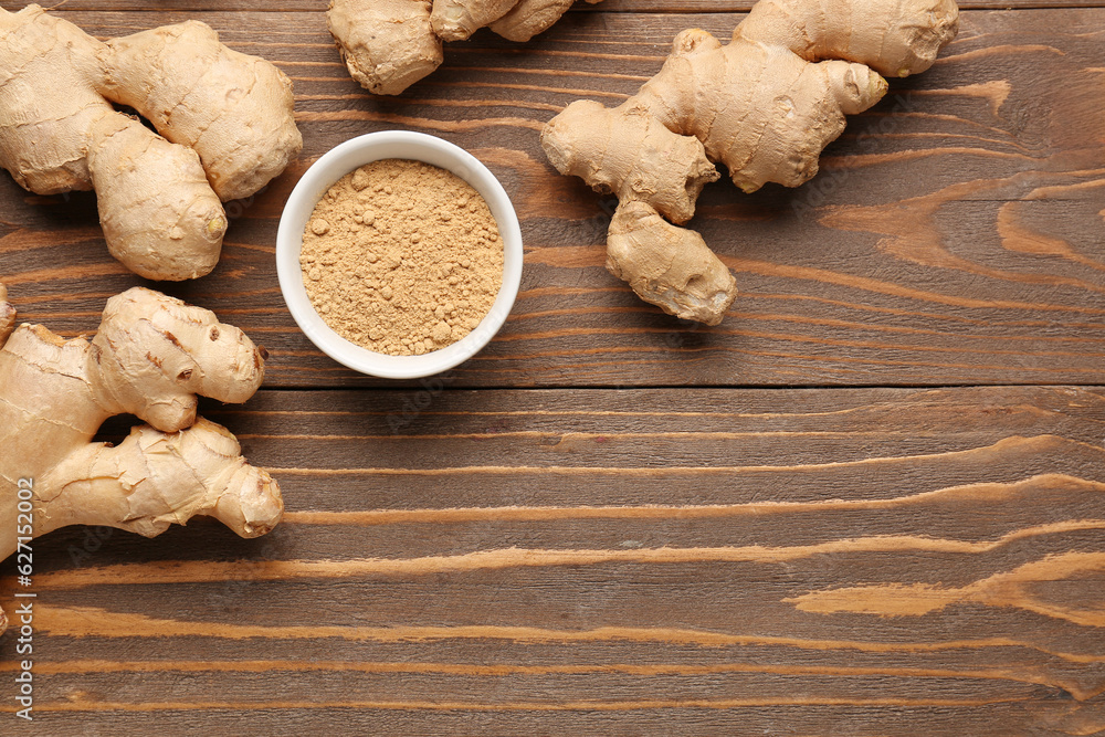 Fresh ginger roots and bowl with dried powder on wooden background