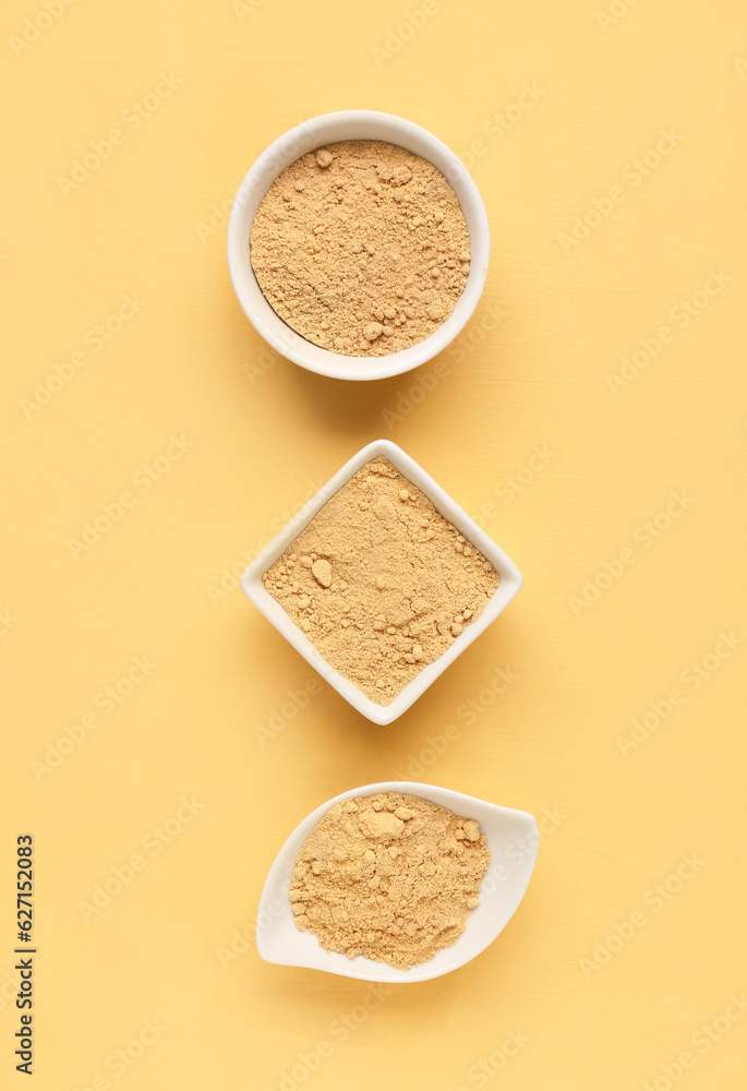 Bowls with ginger powder on yellow background