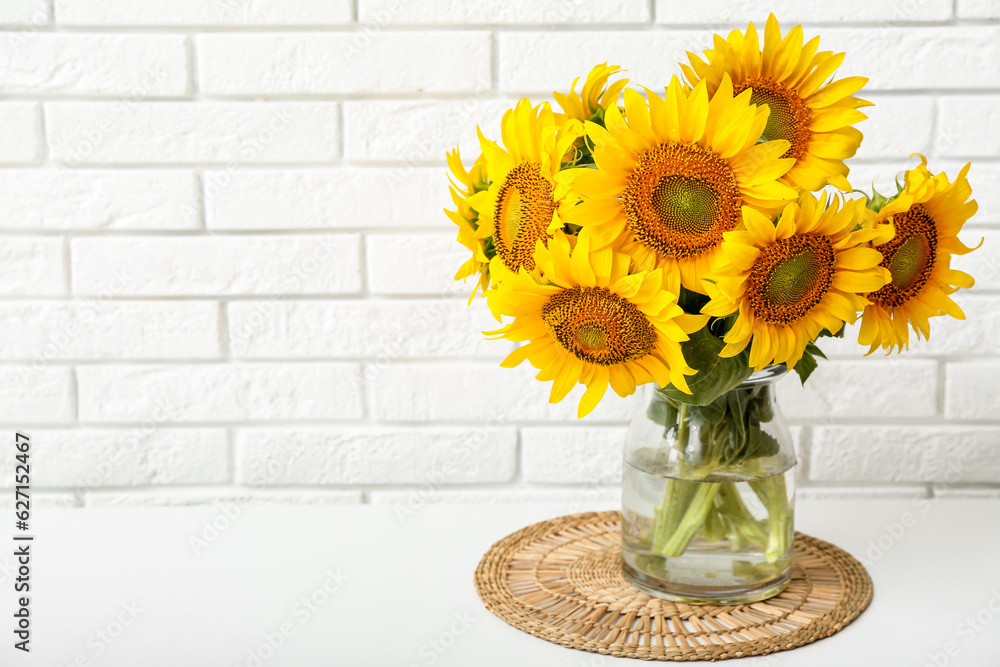 Vase with beautiful sunflowers on table near light brick wall in room, closeup