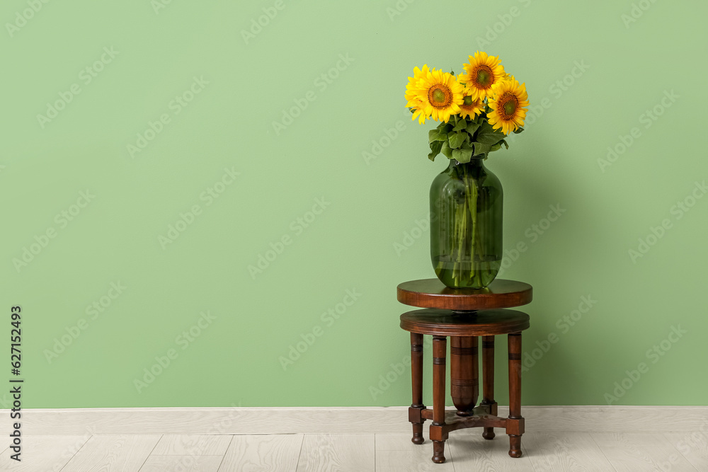 Vase with beautiful sunflowers on stool near green wall in room