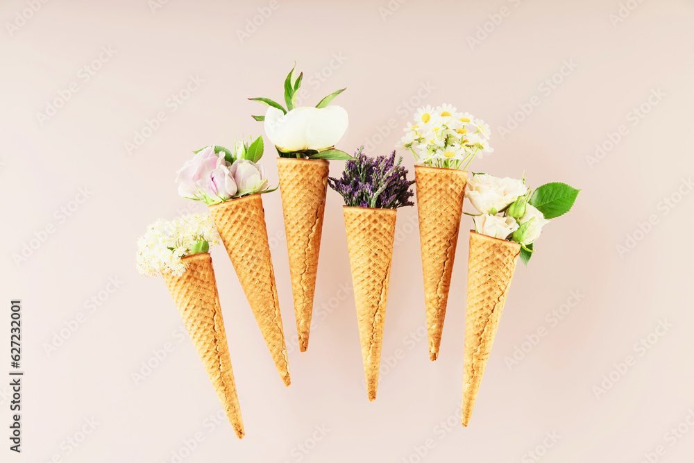 Flat-lay of waffle cones with flowers over pastel light pink background, top view