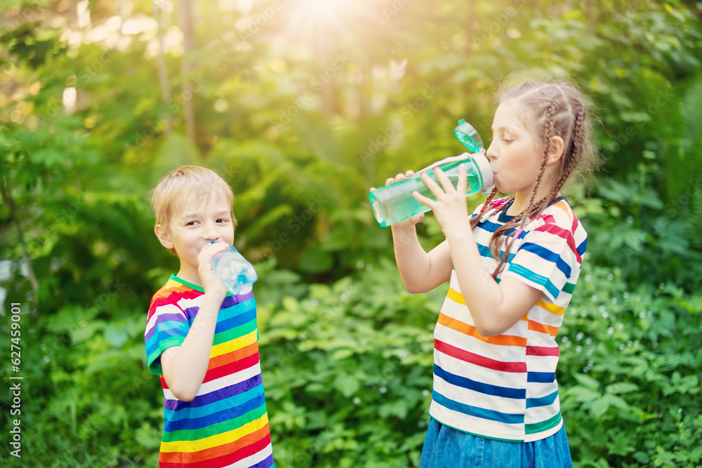 Children with bottles of water in their hands standing outdoors and drinking.