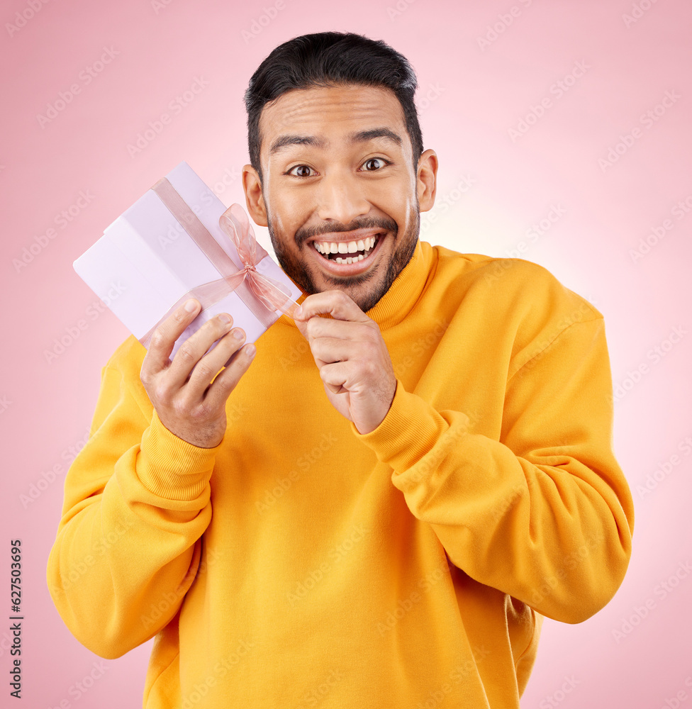 Young man, gift box and studio portrait with excited smile, ribbon and open for celebration by pink 