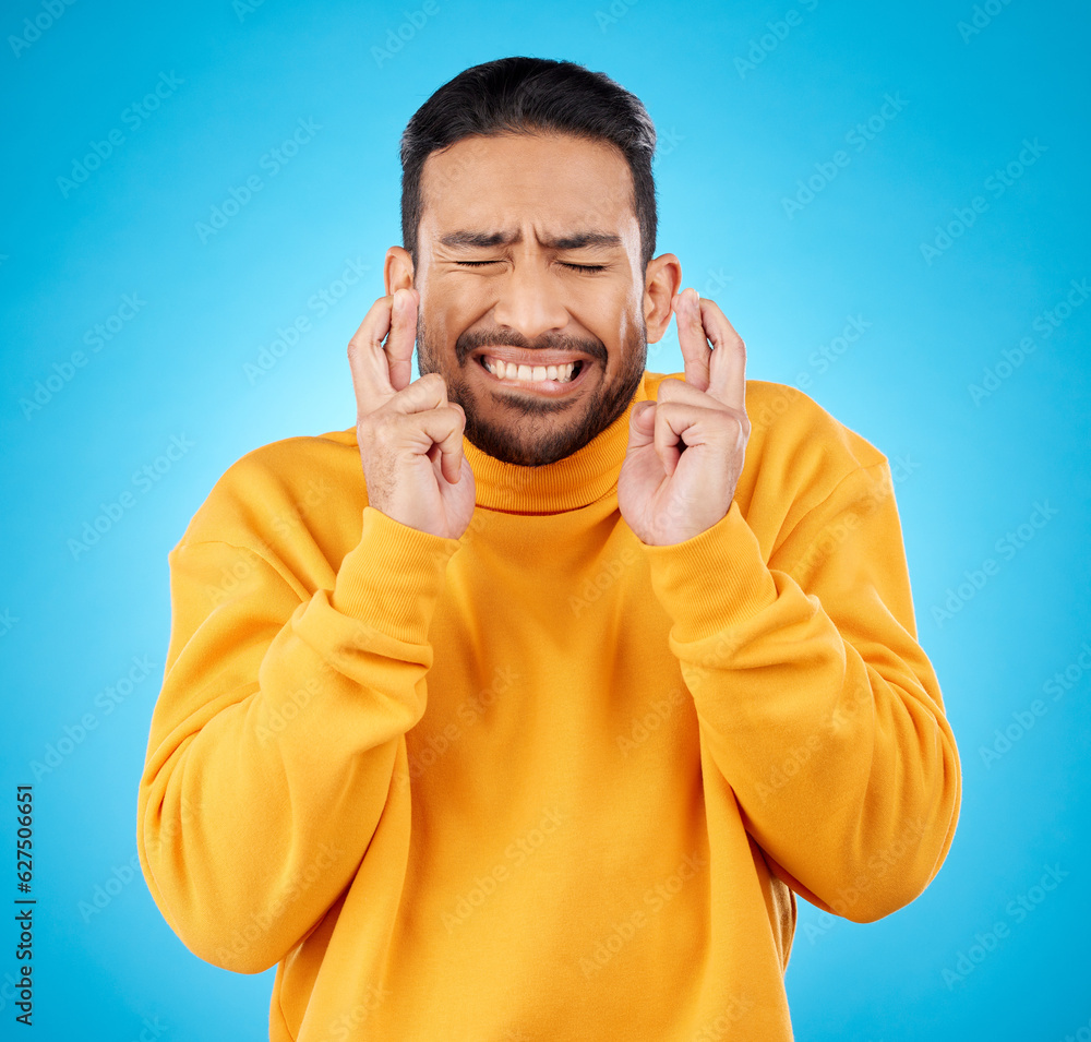 Nervous, eyes closed and fingers crossed by asian man with anxiety in studio for news, feedback or r