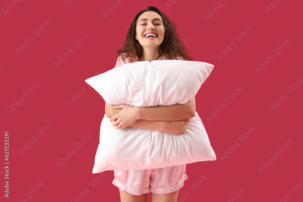 Young brunette woman in pajamas with pillow on pink background