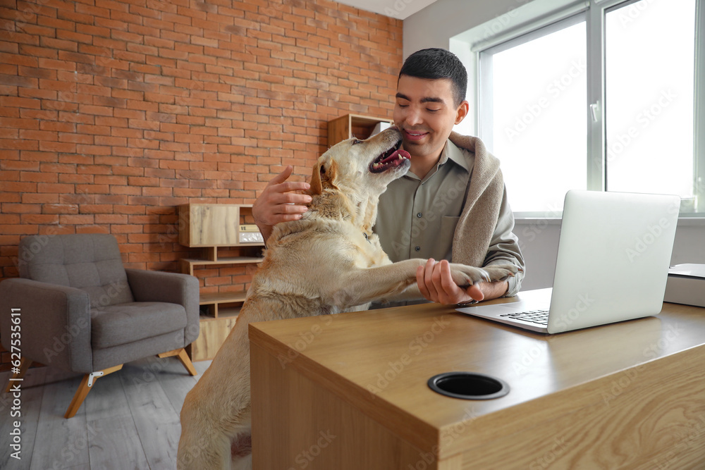 Young man with cute Labrador dog at table in office