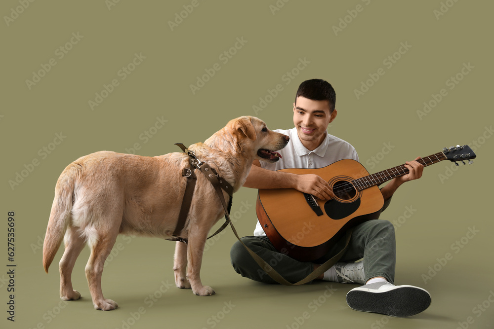 Young man with cute Labrador dog playing guitar on green background