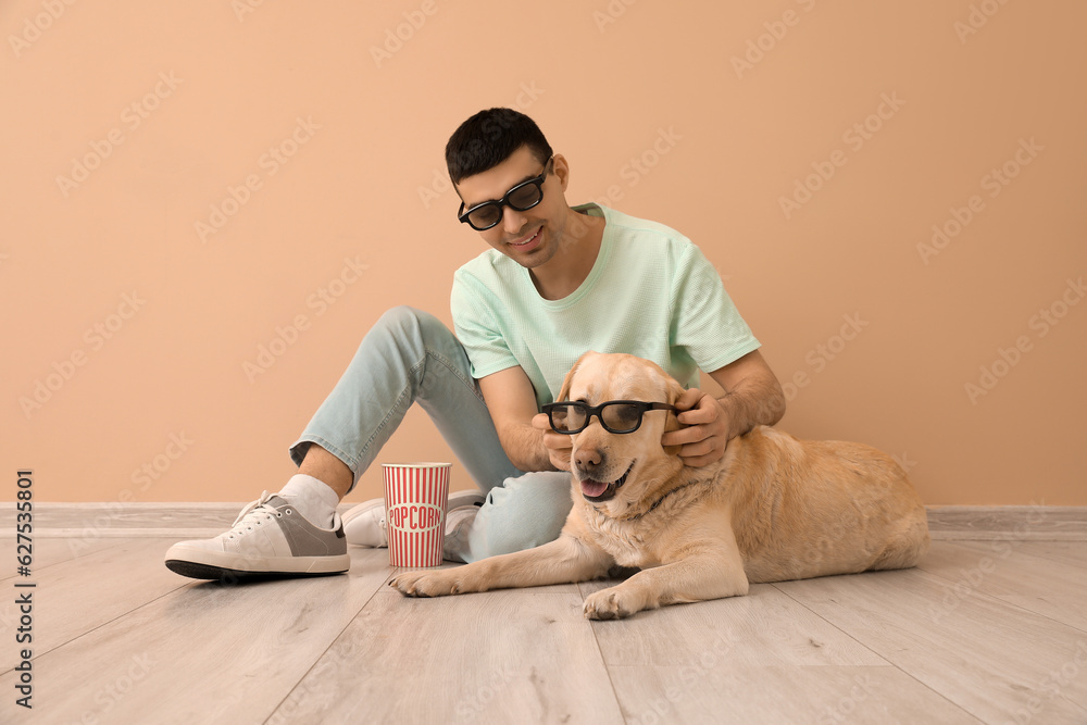 Young man and Labrador dog in 3D glasses with popcorn sitting near beige wall