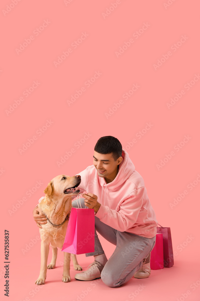 Young man with shopping bags and cute Labrador dog on pink background