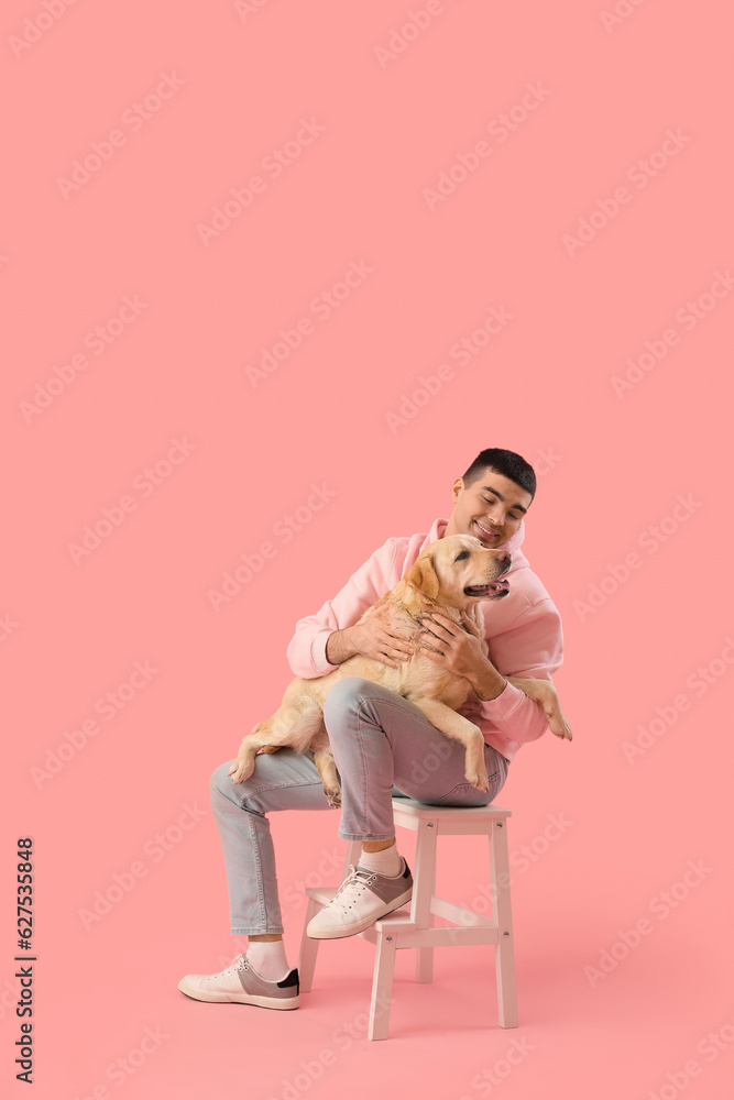 Young man with cute Labrador dog sitting on stepladder against pink background