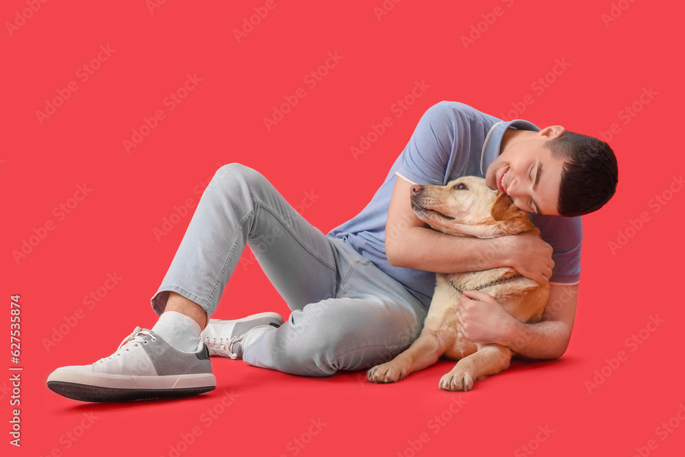 Young man hugging cute Labrador dog on red background