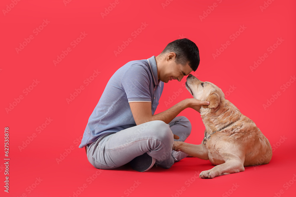 Young man with cute Labrador dog sitting on red background