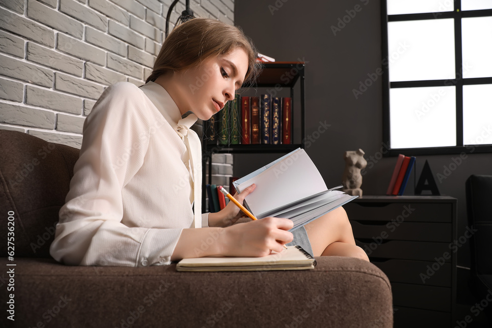 Young businesswoman reading book and making notes in office