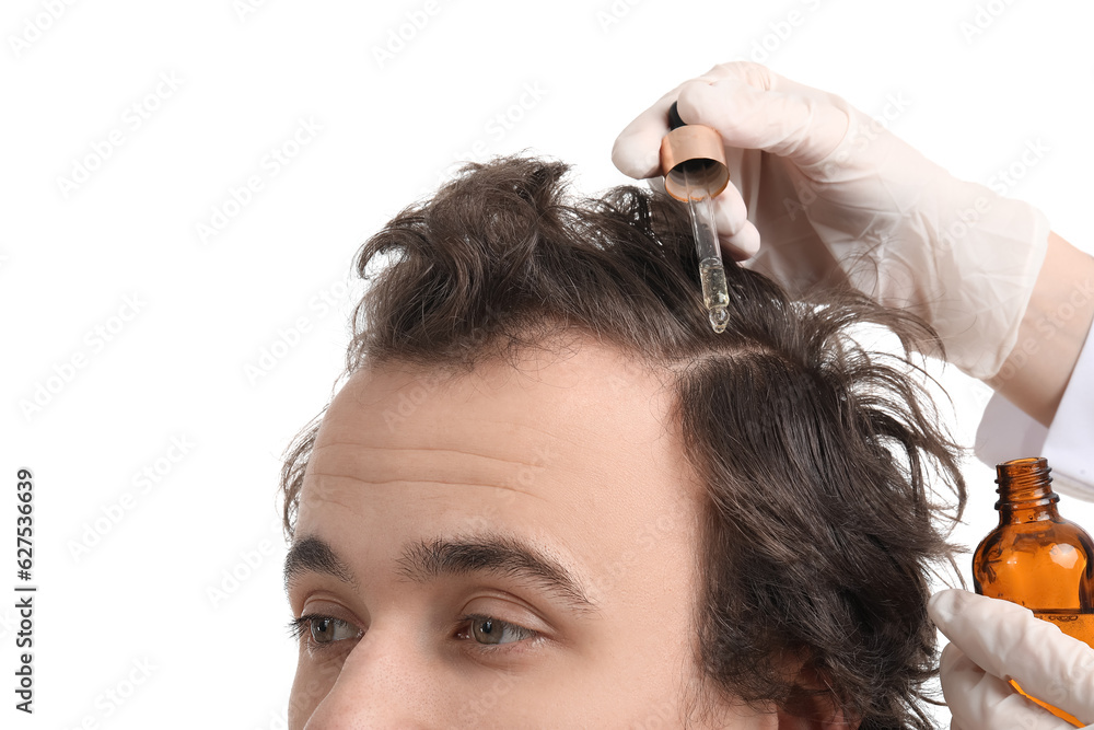 Young man receiving serum for hair growth on white background, closeup