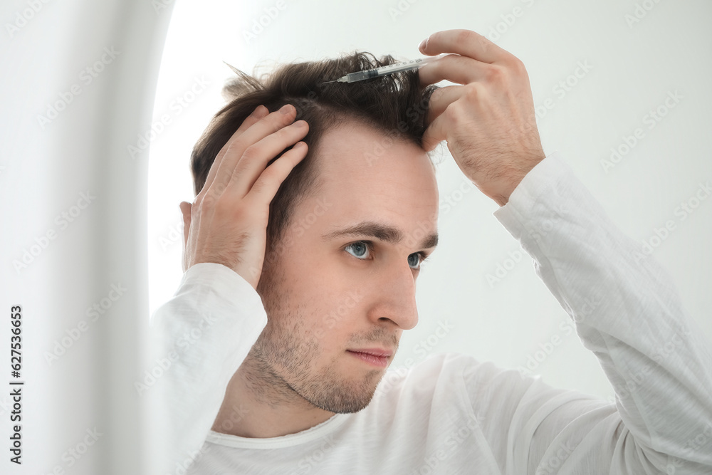 Young man with injection for hair growth near mirror in bathroom, closeup