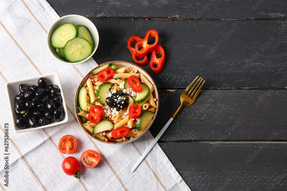 Bowl with tasty pasta salad and ingredients on dark wooden background