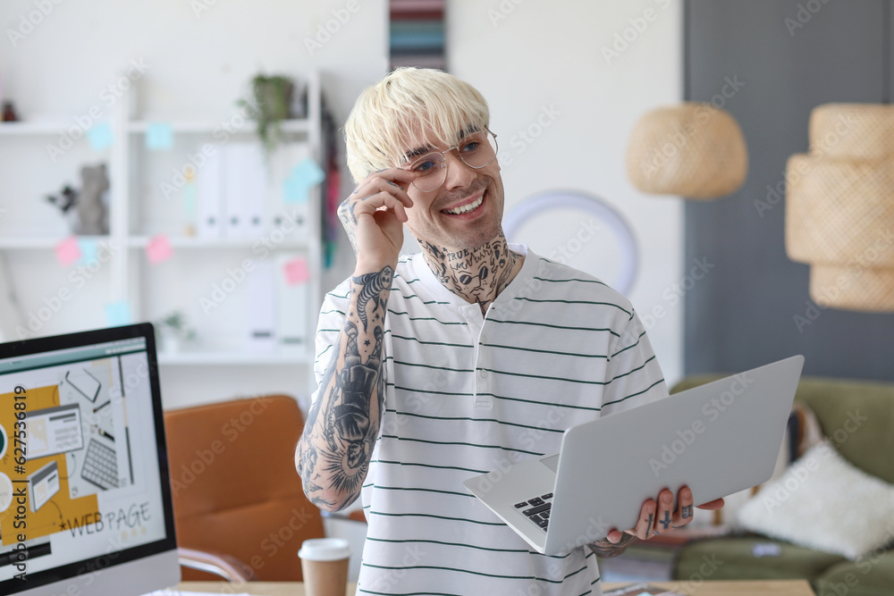 Tattooed graphic designer working with laptop in office