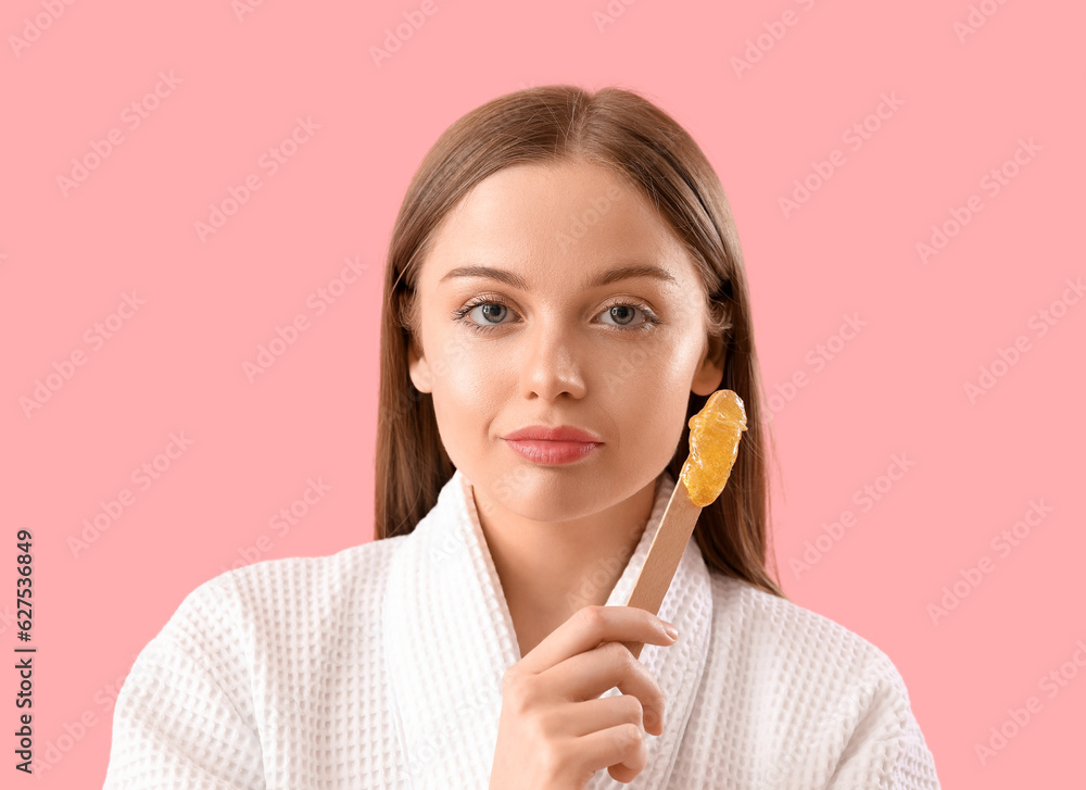 Young woman holding spatula with sugaring paste on pink background