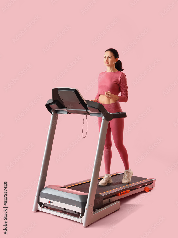 Beautiful woman training on treadmill against pink background