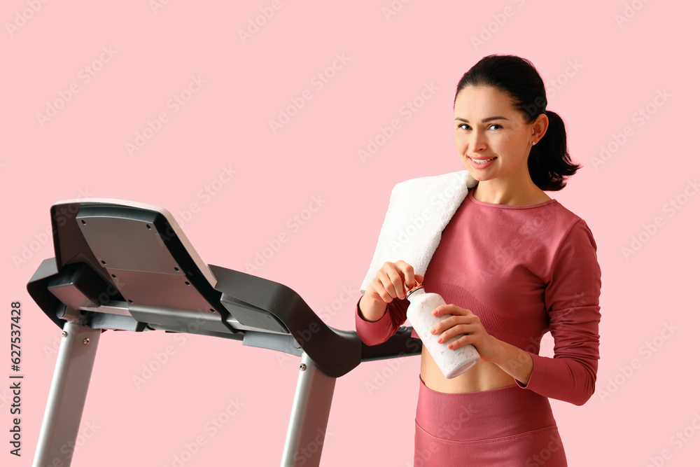 Beautiful woman with bottle of water and treadmill on pink background