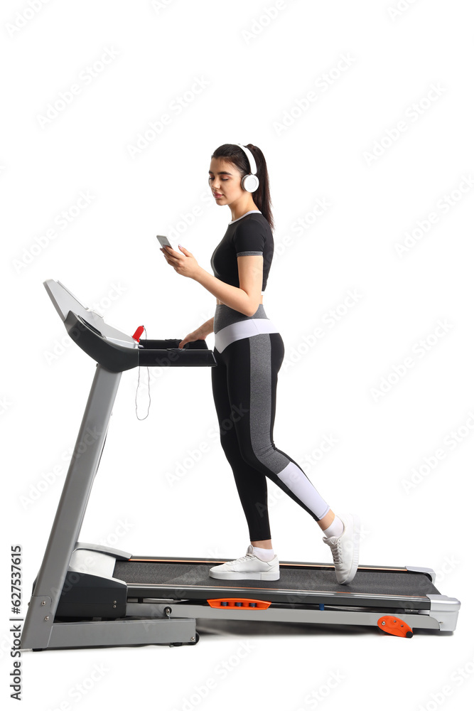 Sporty young woman in headphones using mobile phone on treadmill against white background