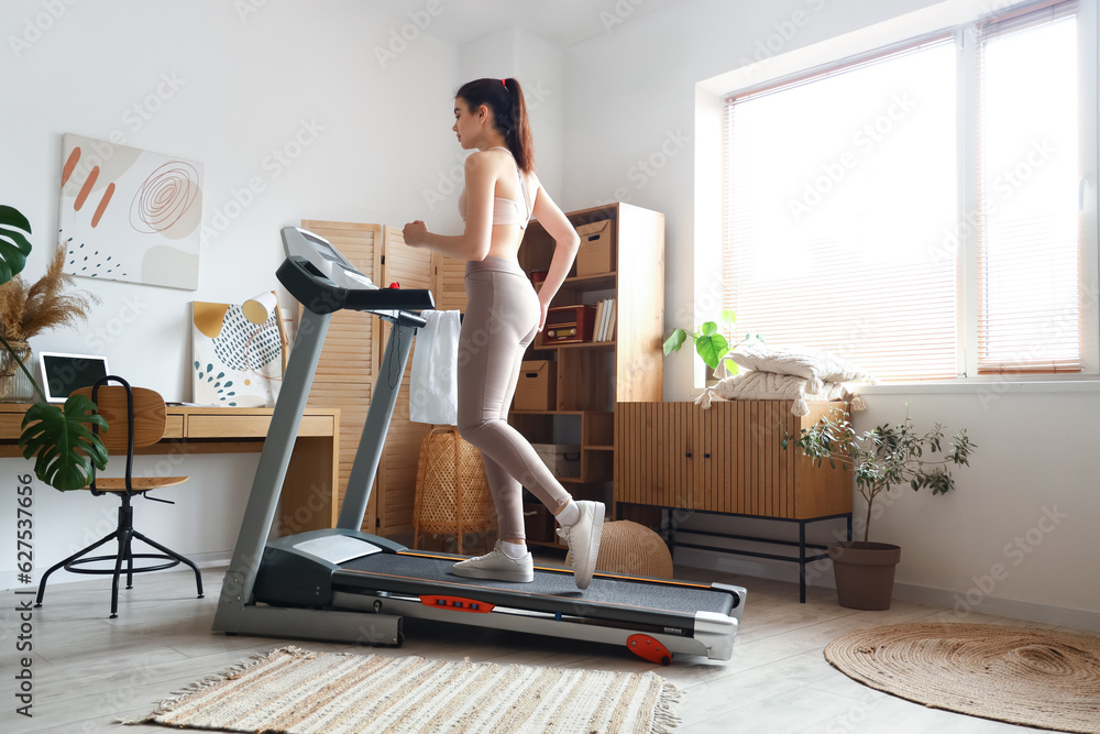 Sporty young woman training on treadmill at home