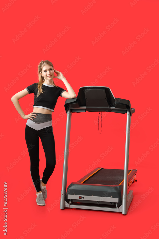 Sporty young woman with treadmill on red background