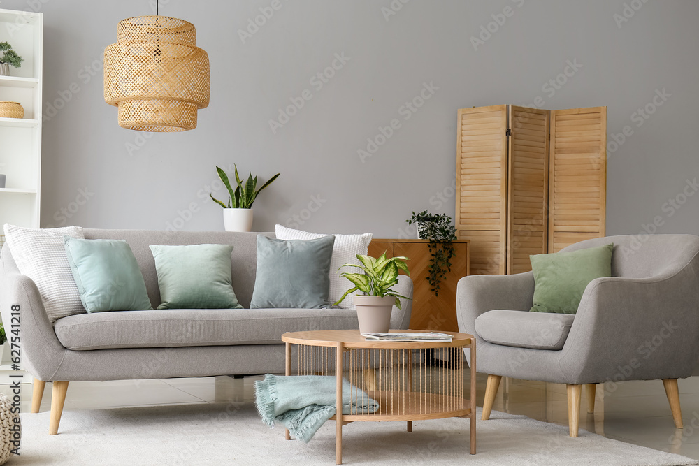 Interior of stylish living room with grey sofa, armchair and houseplant on coffee table