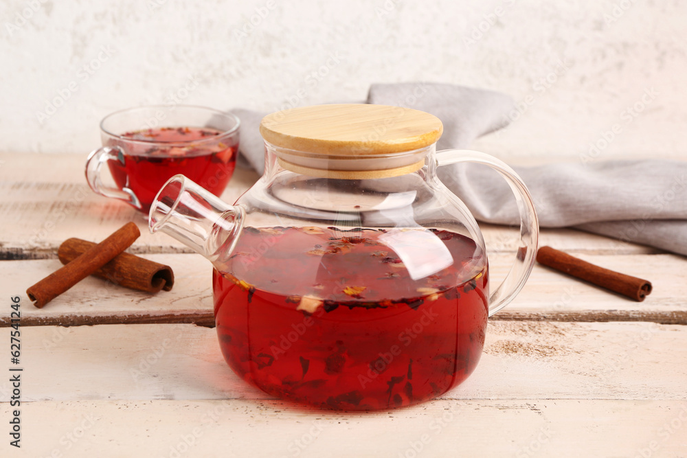 Transparent teapot and cup with fruit tea on white wooden table