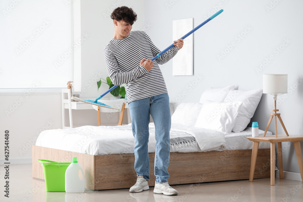 Young man with mop having fun in bedroom