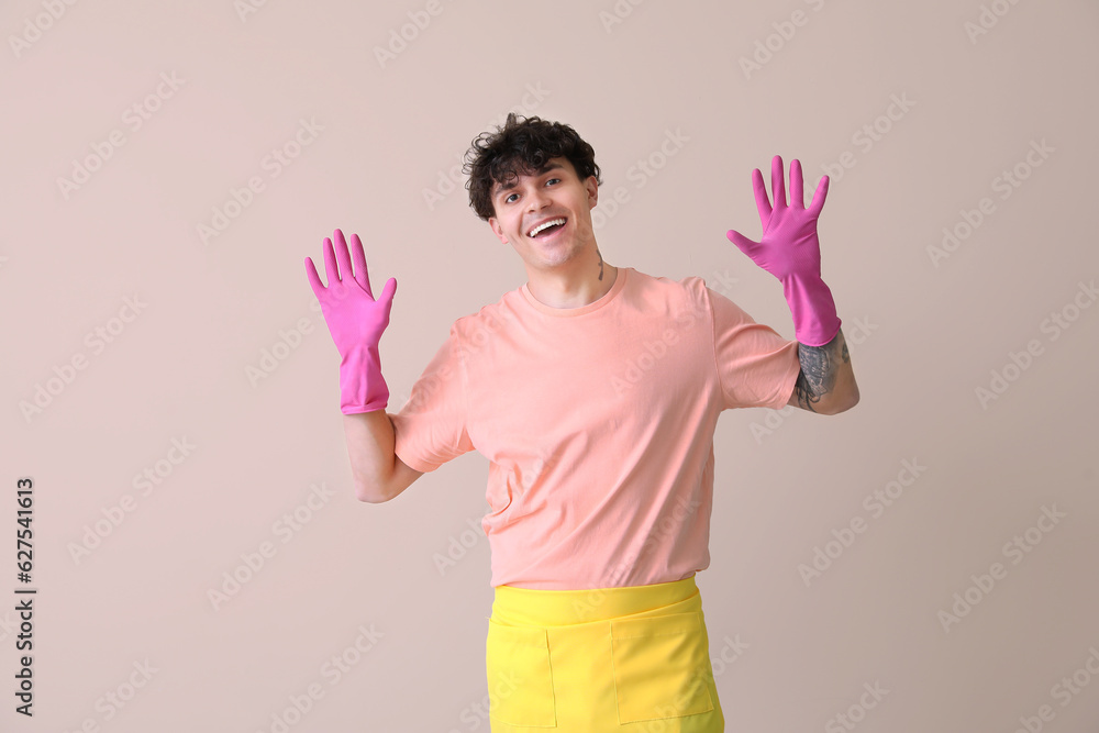 Young man in rubber gloves on beige background