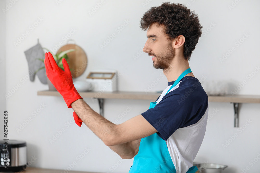 Young man putting rubber gloves in kitchen