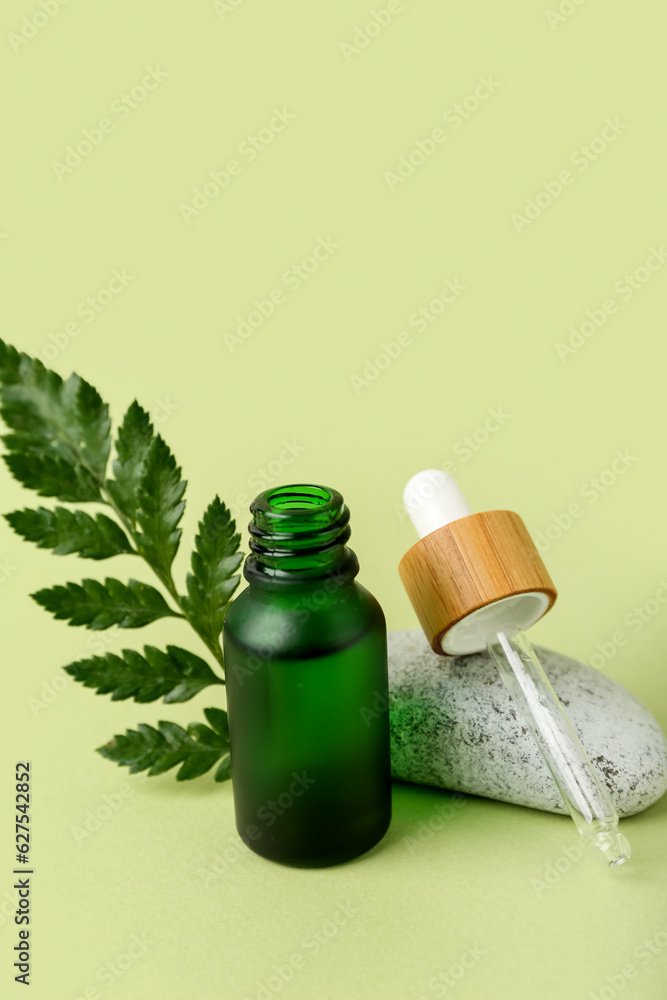 Open bottle of cosmetic oil with plant twig and stone on light green background