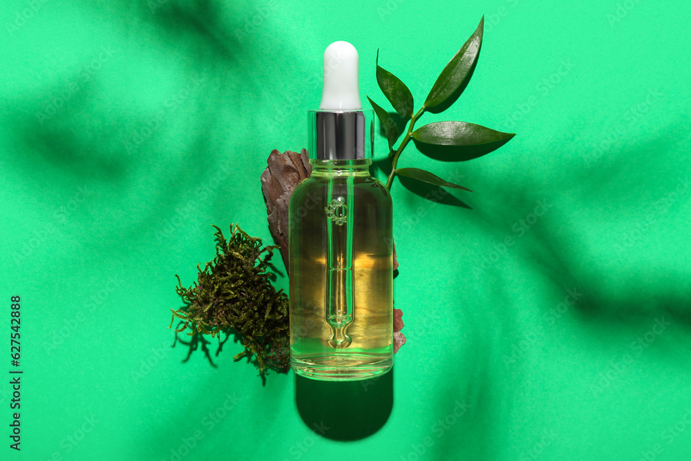 Bottle of cosmetic oil with plant twig, tree bark and moss on green background