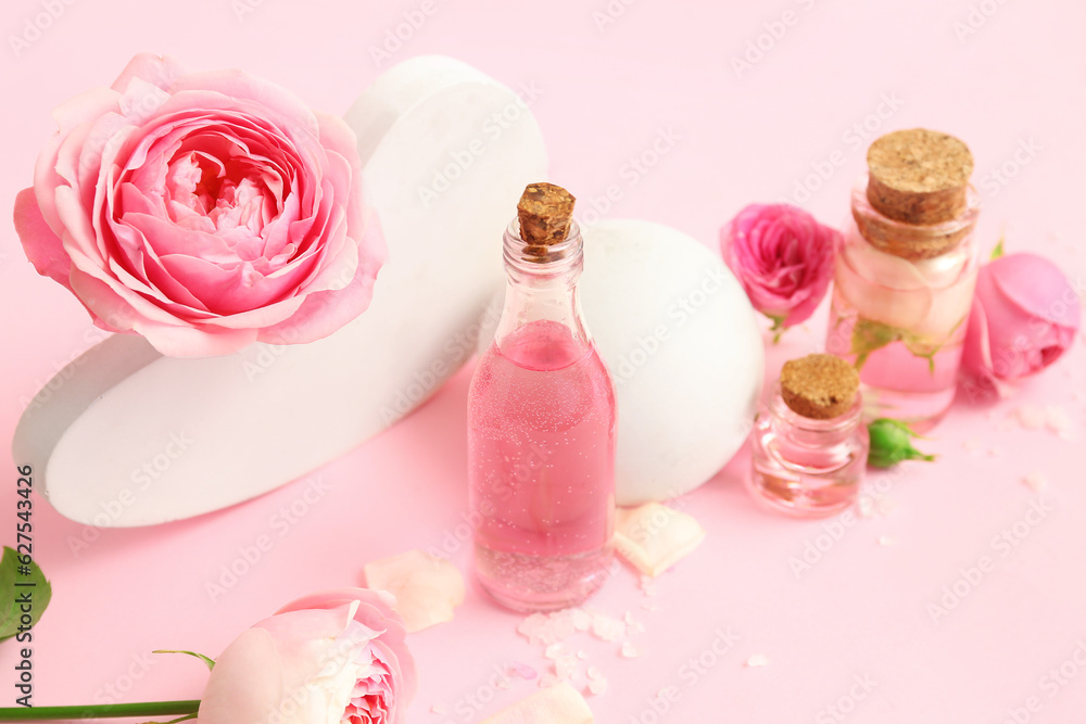 Bottles of cosmetic oil with rose extract and flowers on pink background