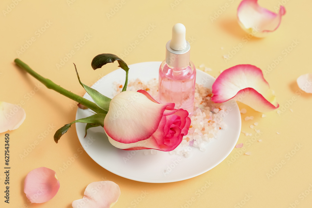 Bottle of cosmetic oil with rose extract and flower on beige table