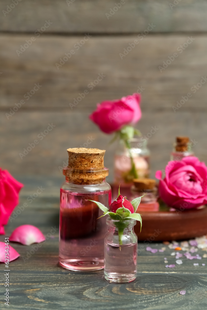 Bottles of cosmetic oil with rose extract and flowers on wooden table