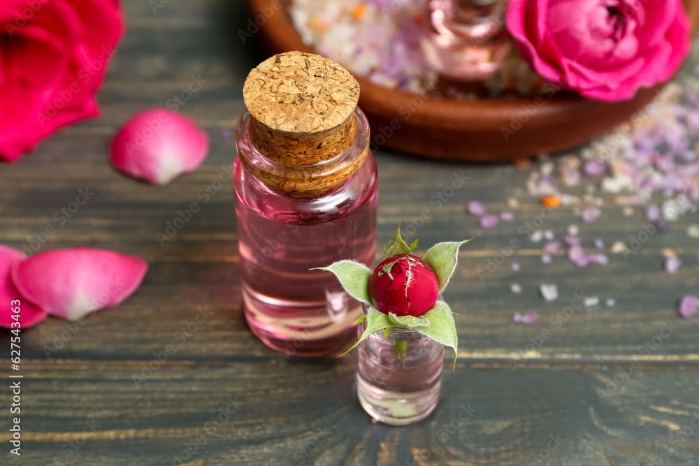 Bottles of cosmetic oil with rose extract and flowers on wooden table