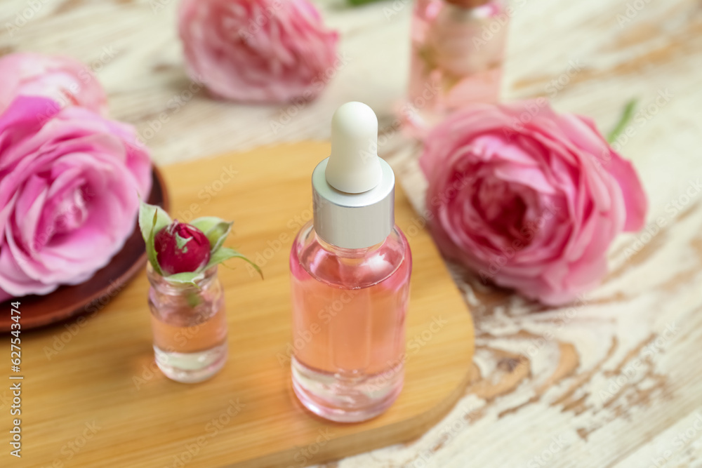 Bottles of cosmetic oil with rose extract and flowers on light wooden table