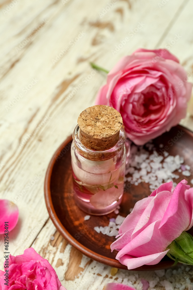 Bottle of cosmetic oil with rose extract and flowers on light wooden table