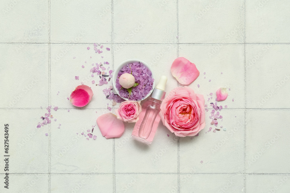 Bottle of cosmetic oil with rose extract and flowers on white tile background